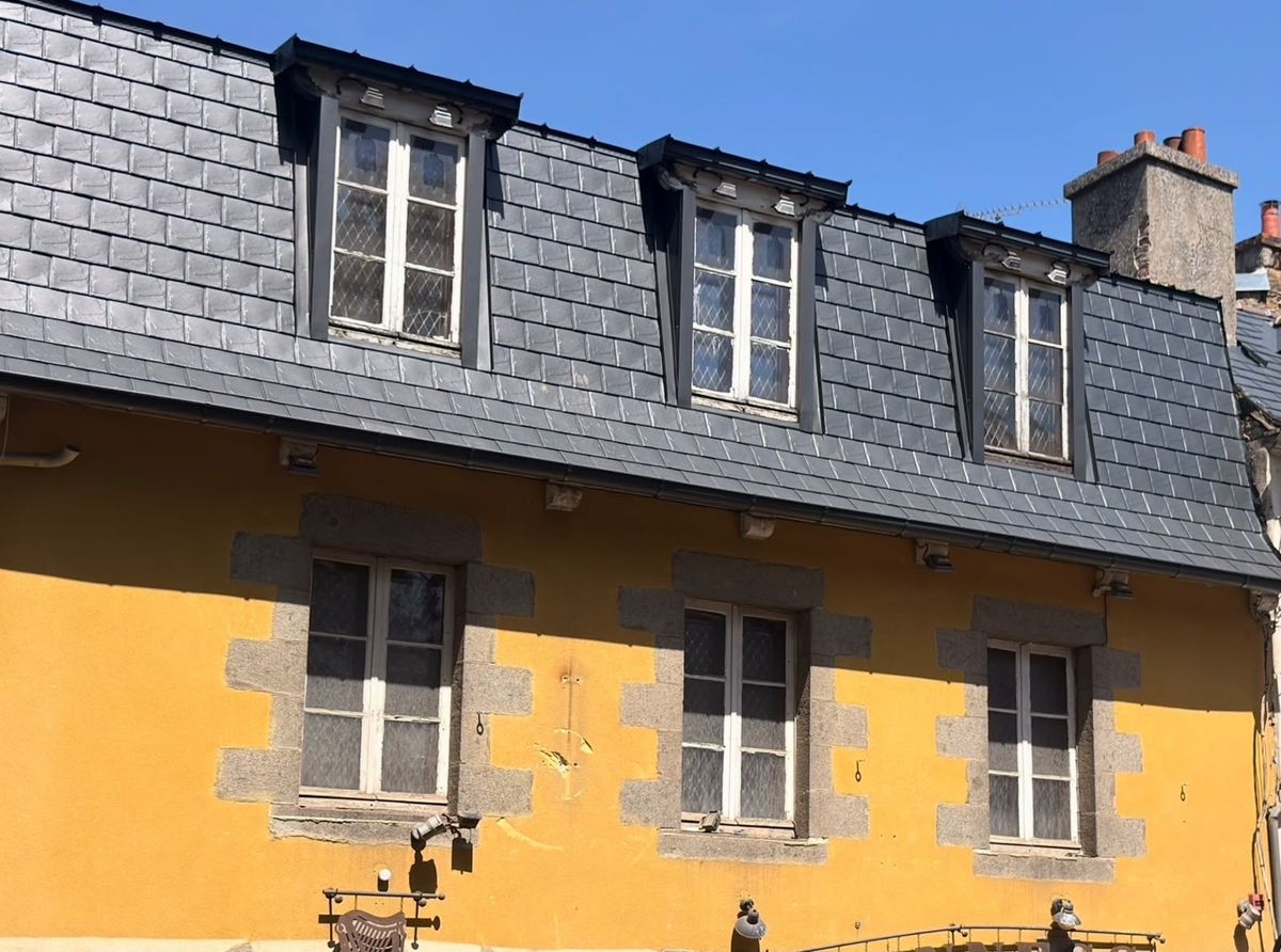 Façade jaune surmontée d'une toiture neuve en tuiles aluminium et de trois lucarnes habillées