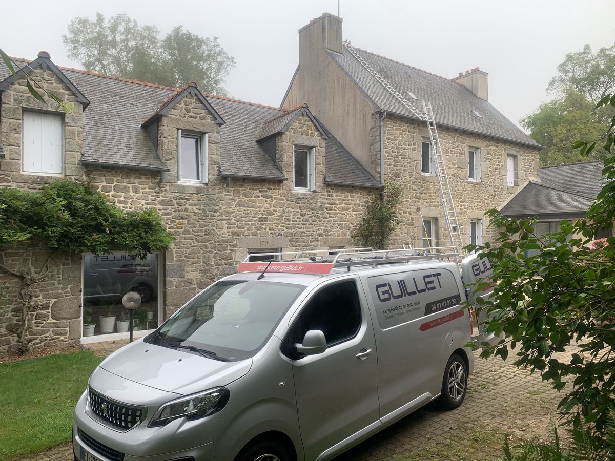 Longère en pierre à lucarnes, échelle de couvreur dressée jusqu'au faîtage et véhicules de l'entreprise dans la cour